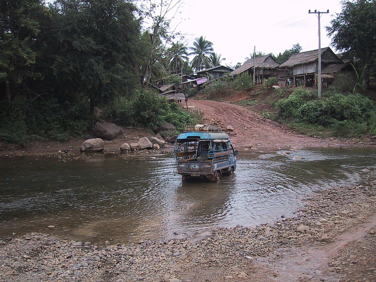 A light truck crossing a shallow river on a rural road in Laos, water below the wheel hubs